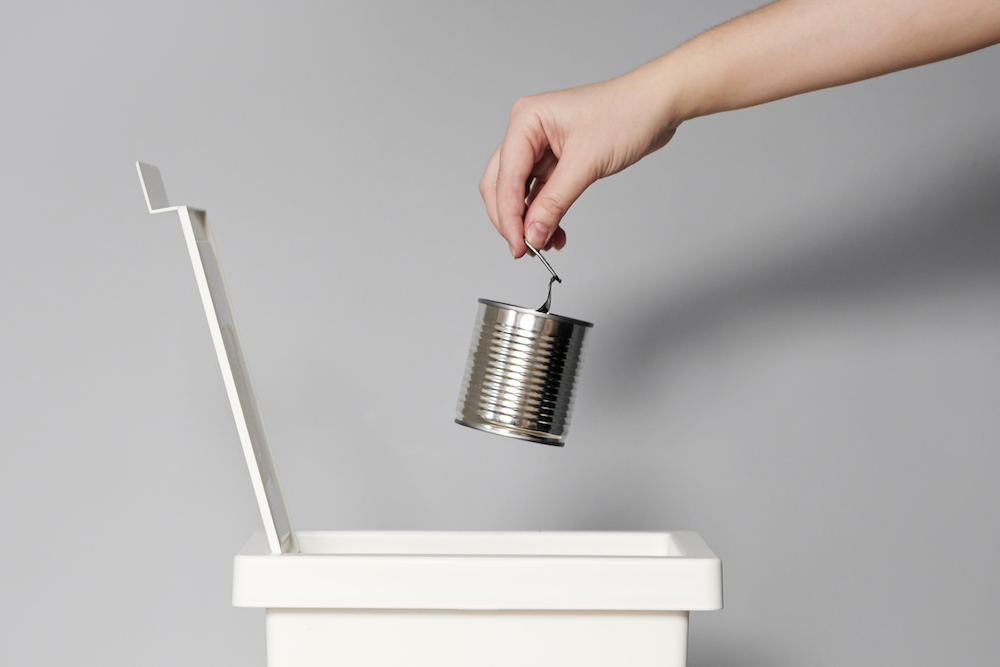 Hand puts empty tin can in the trash bin for recycling.Activist taking care of environment, sorting tin can waste to proper recycling bin.Concept of Recycling plastic and ecology.
